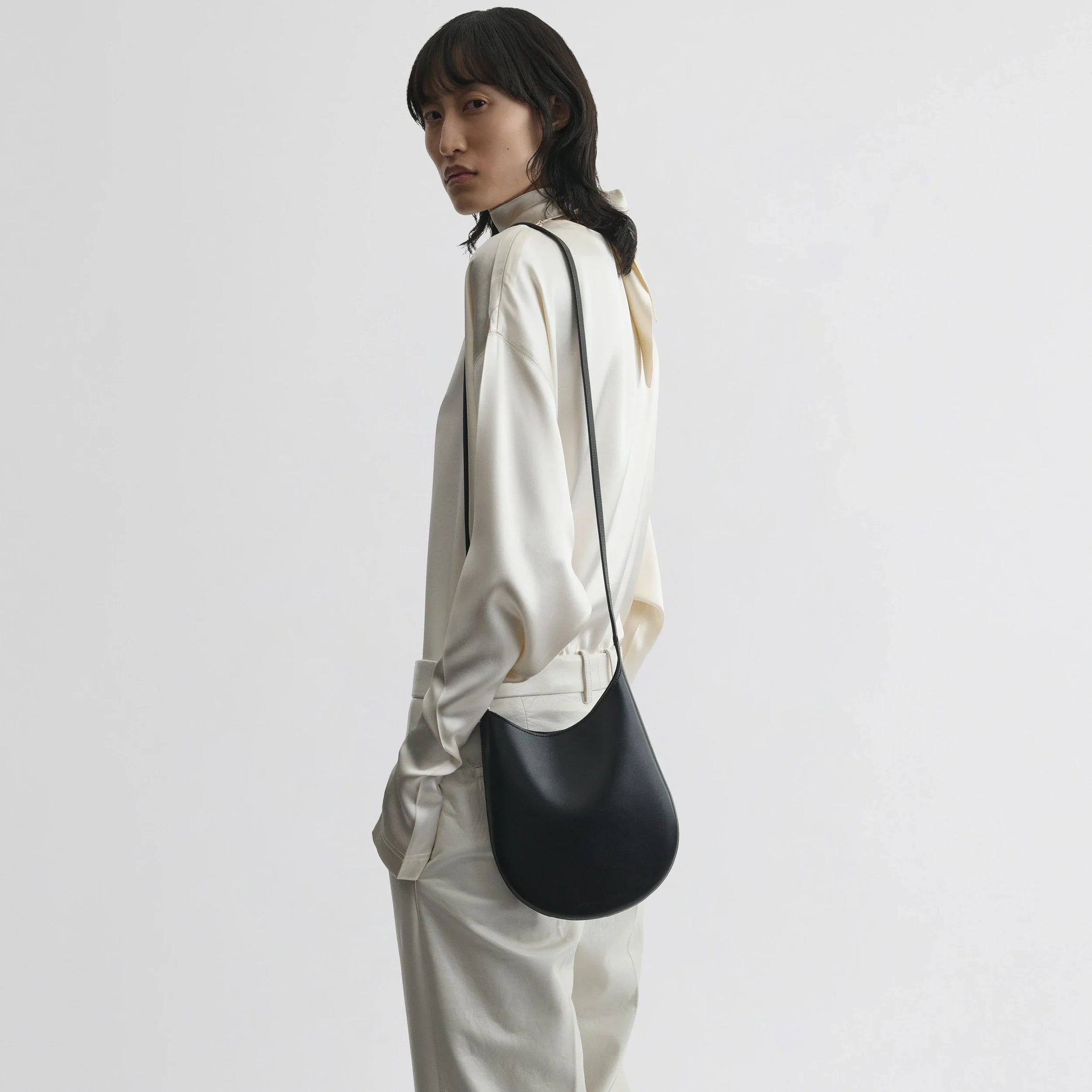 Side view of model wearing mini bean sling in black leather.