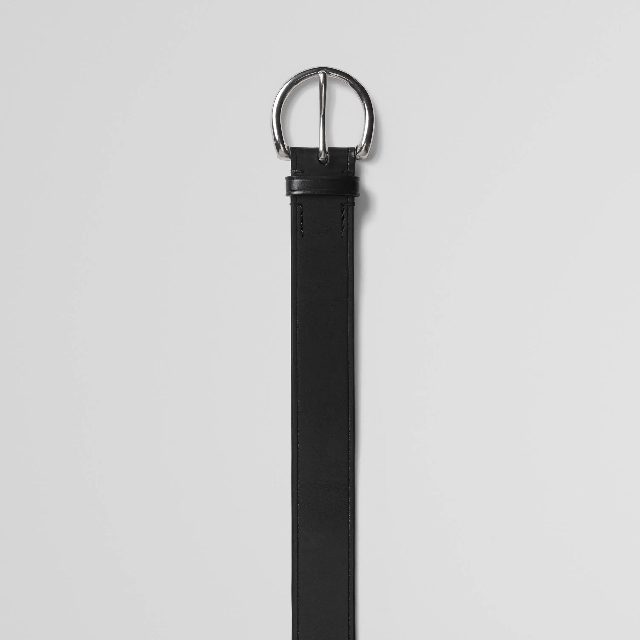 Detail view of round buckle belt in black calf leather.