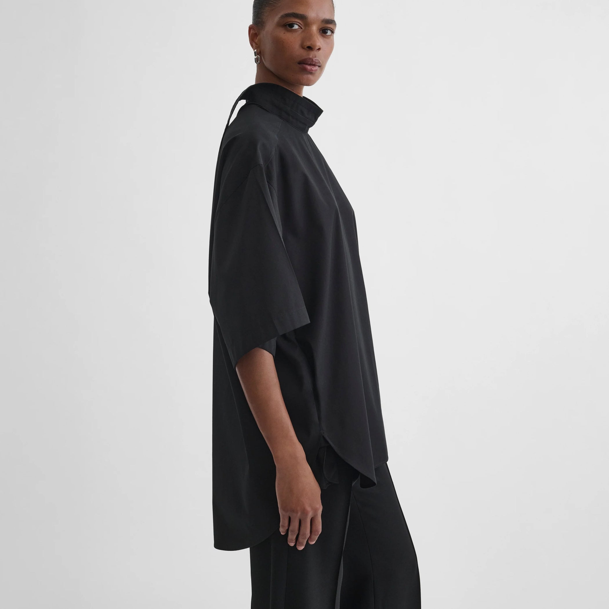 Side view of model wearing tie neck short sleeve shirt in black cotton