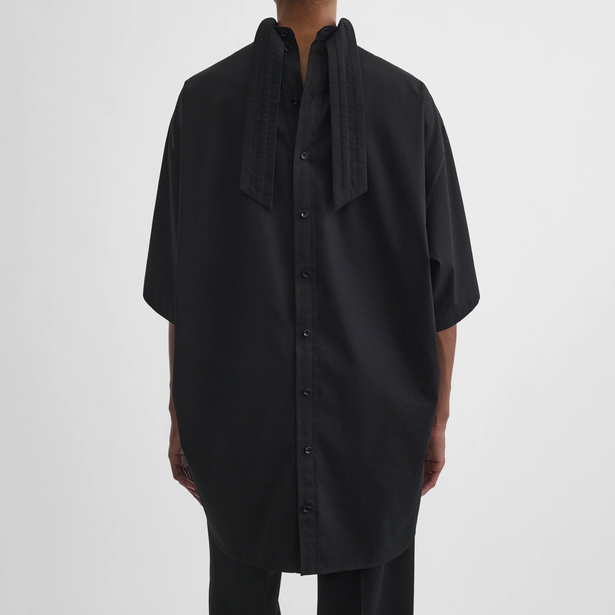 Close up view of model wearing tie neck short sleeve shirt in black cotton