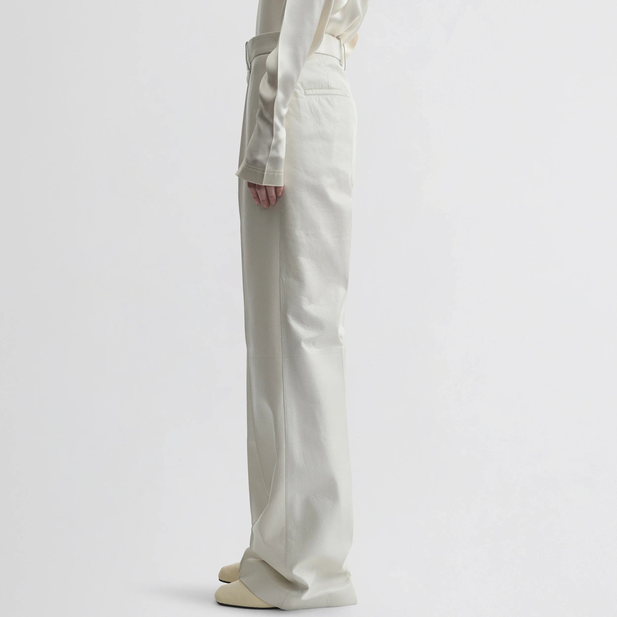 Side view of model wearing boyish trousers in white leather.