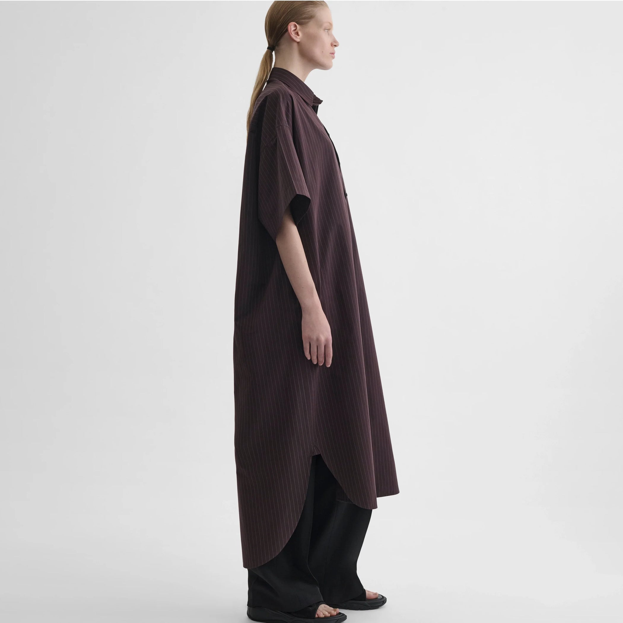 Side full body view of model wearing long shirt dress in black cherry cotton