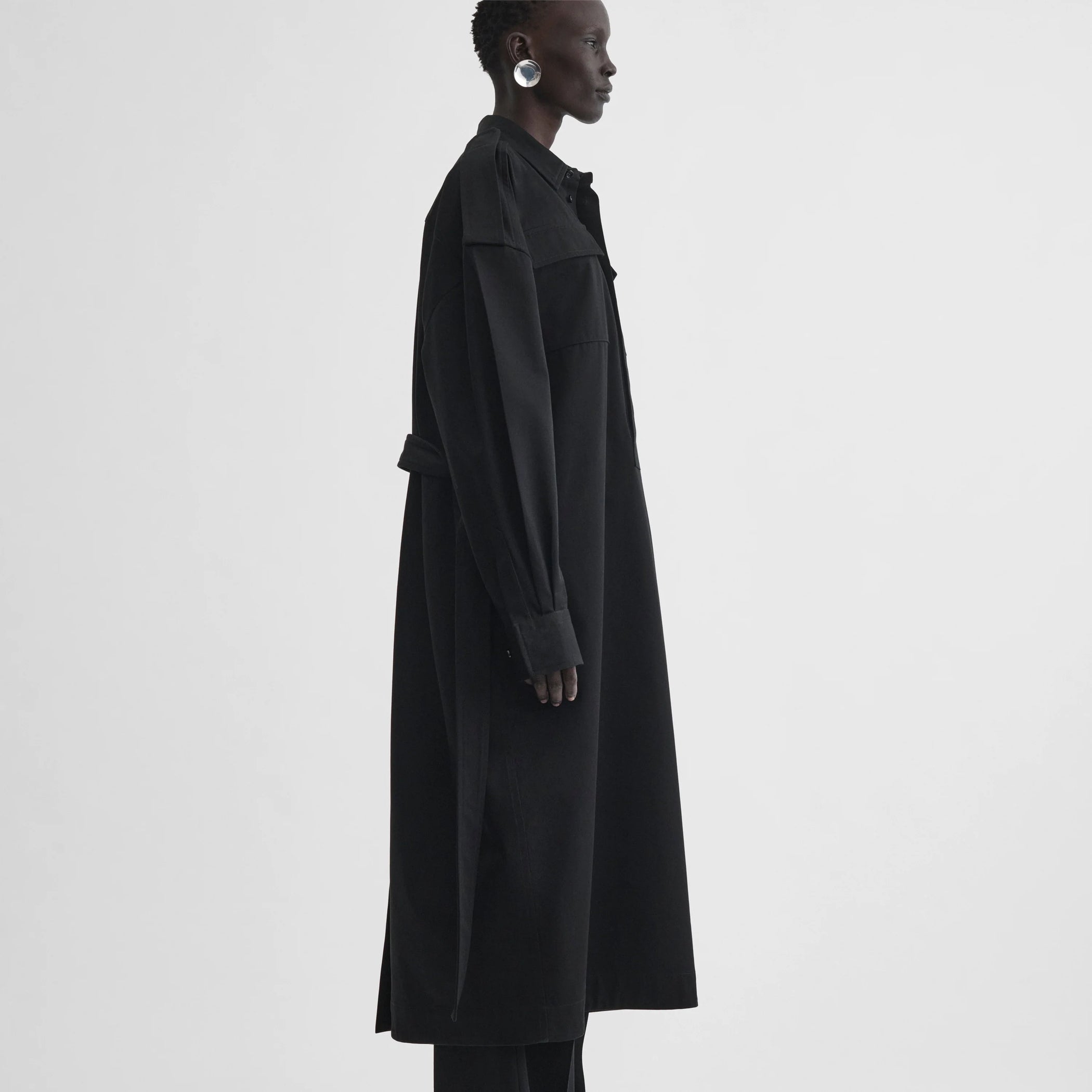 Side full body view of model wearing utility shirt dress in black cotton
