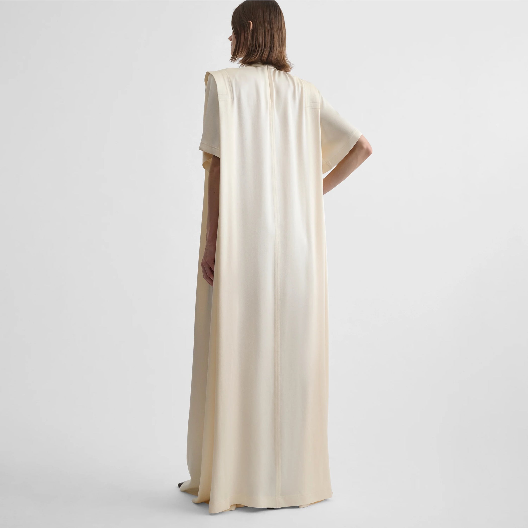 Angled back view of model wearing folded shoulder dress in vanilla satin back crepe