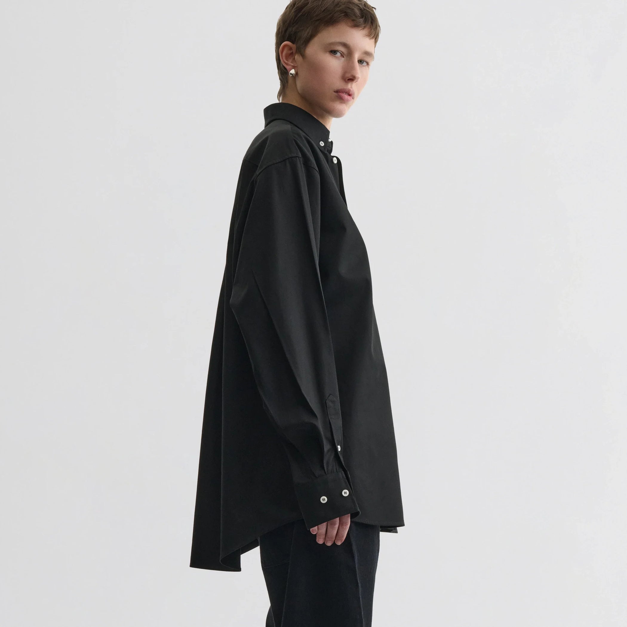 Side view of model wearing button collar shirt in black cotton.