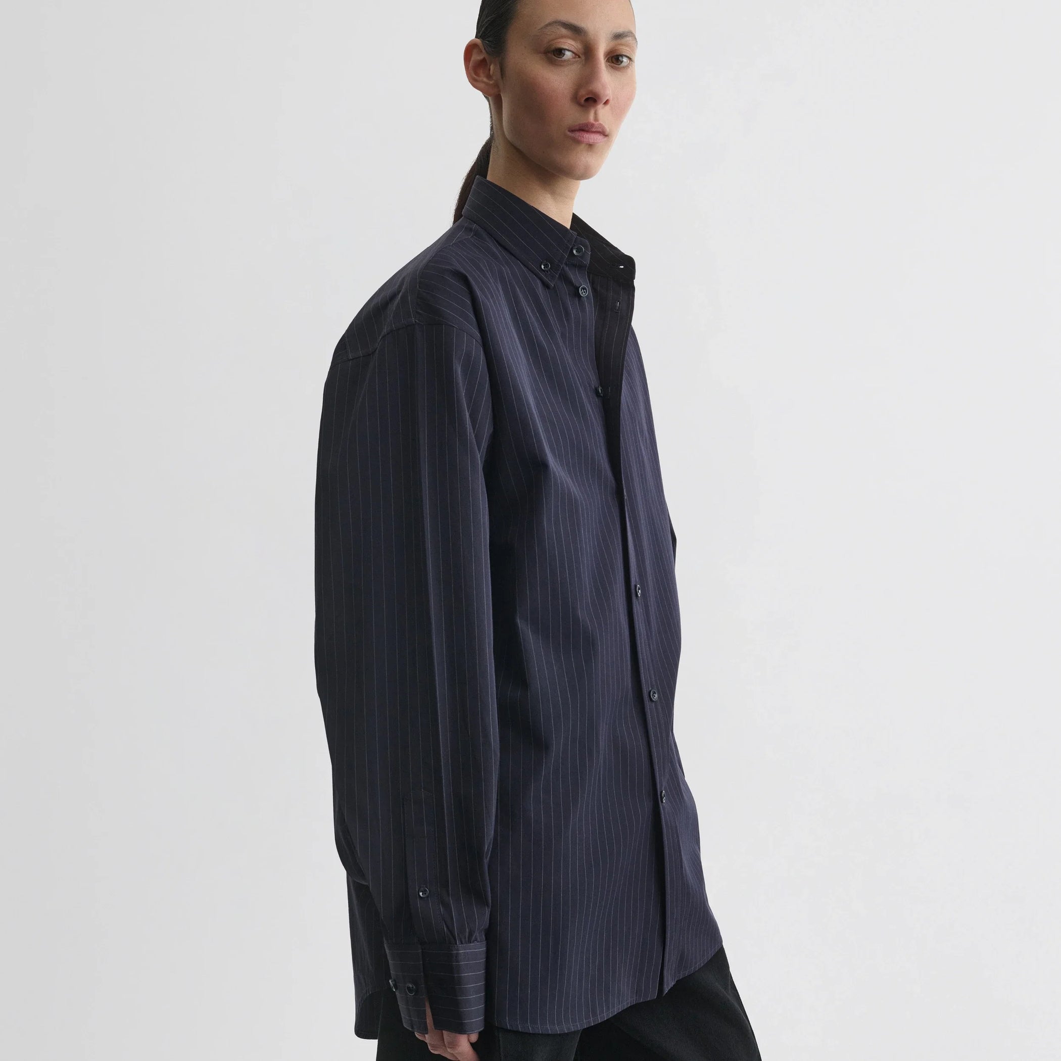 Side view of model wearing button collar shirt in midnight pinstripe cotton.