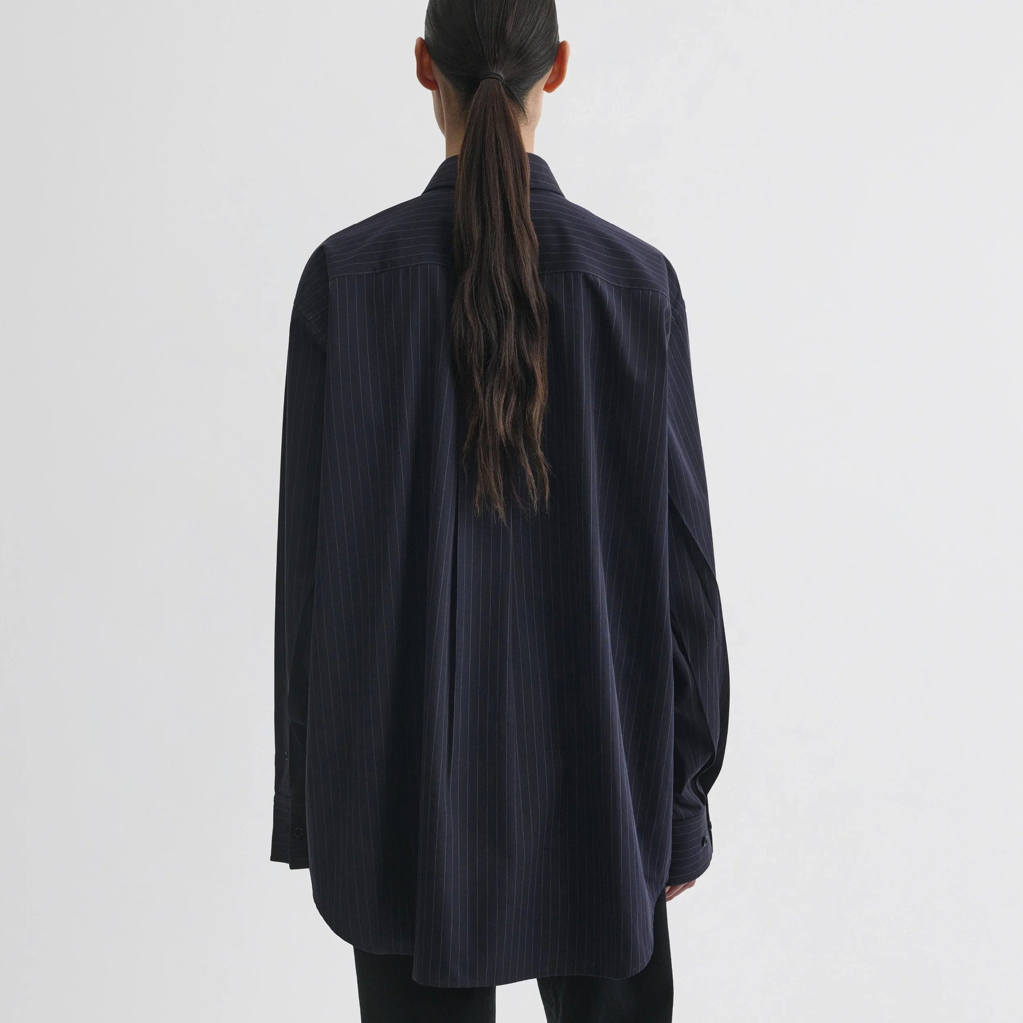 Back view of model wearing button collar shirt in midnight pinstripe cotton.
