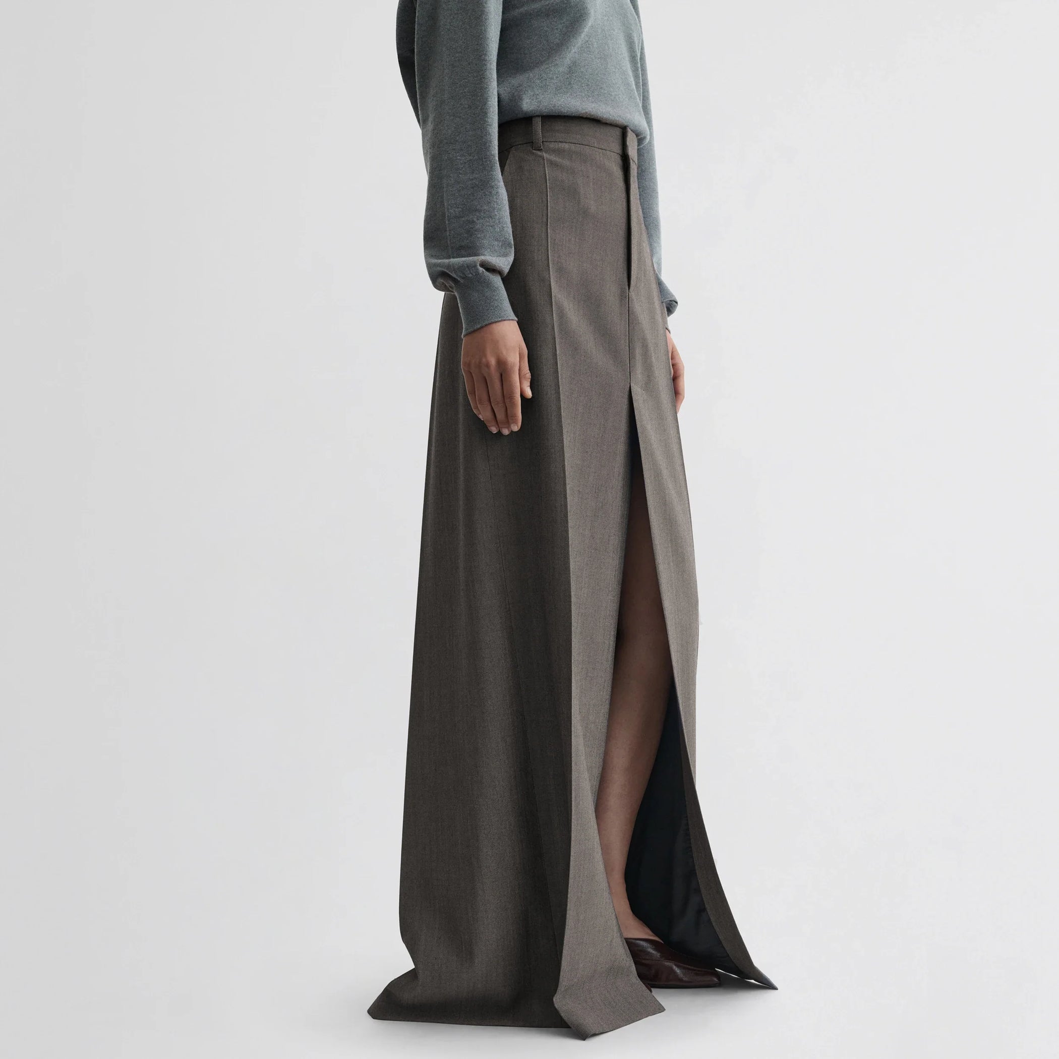 Side view of model wearing double slit tailored skirt in dark taupe wool.