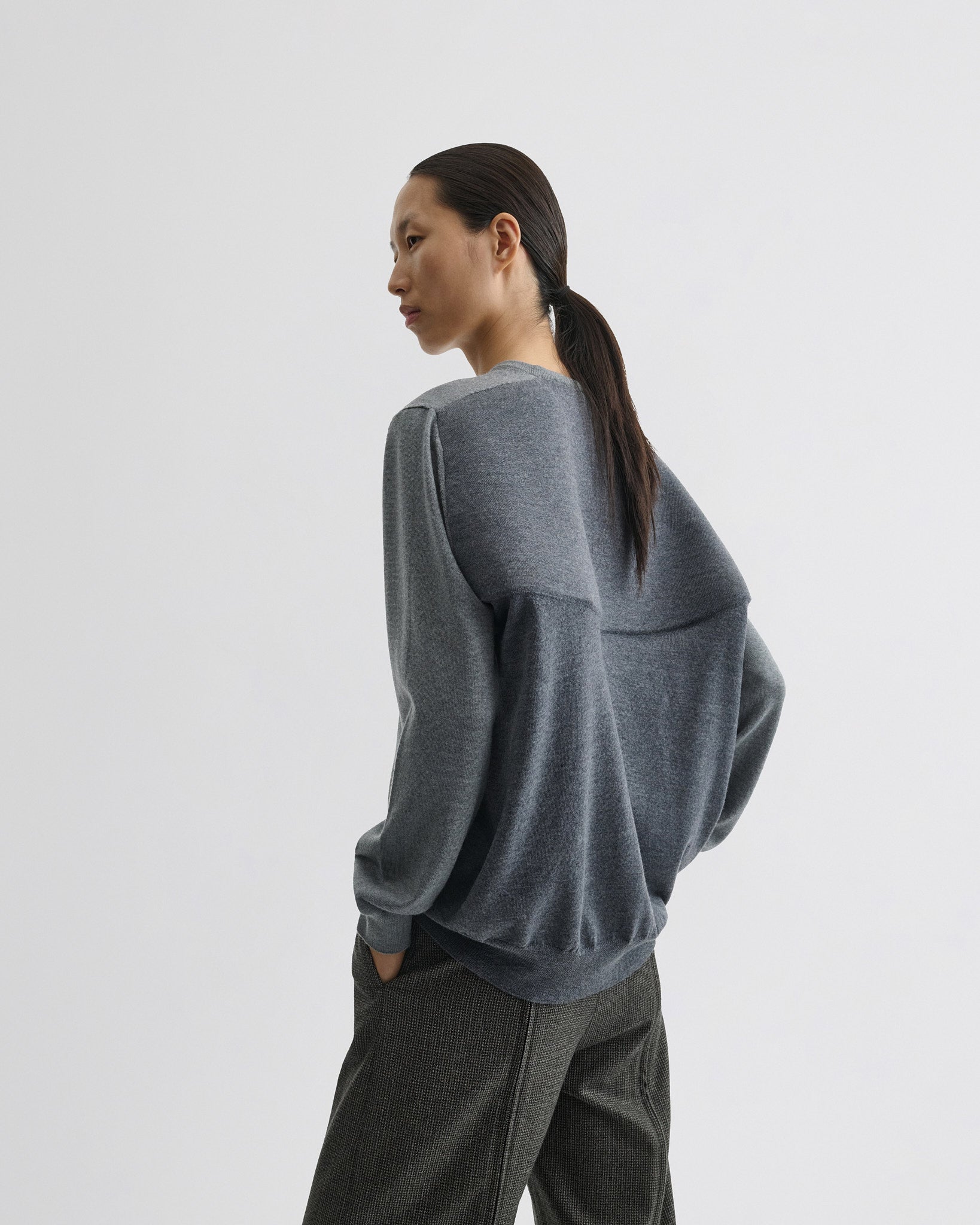 Side view of model wearing backed v-neck sweater in light grey wool.