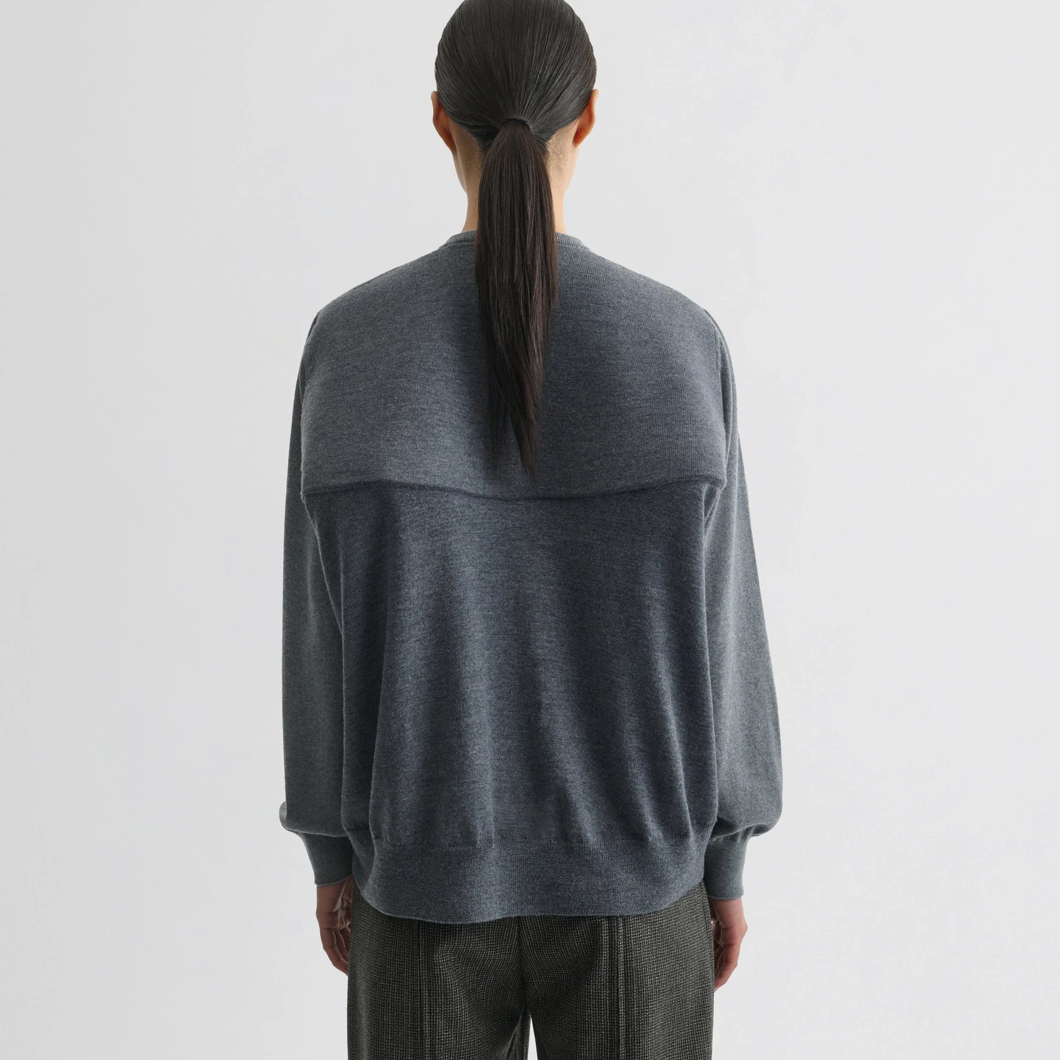Back view of model wearing backed v-neck sweater in light grey wool.