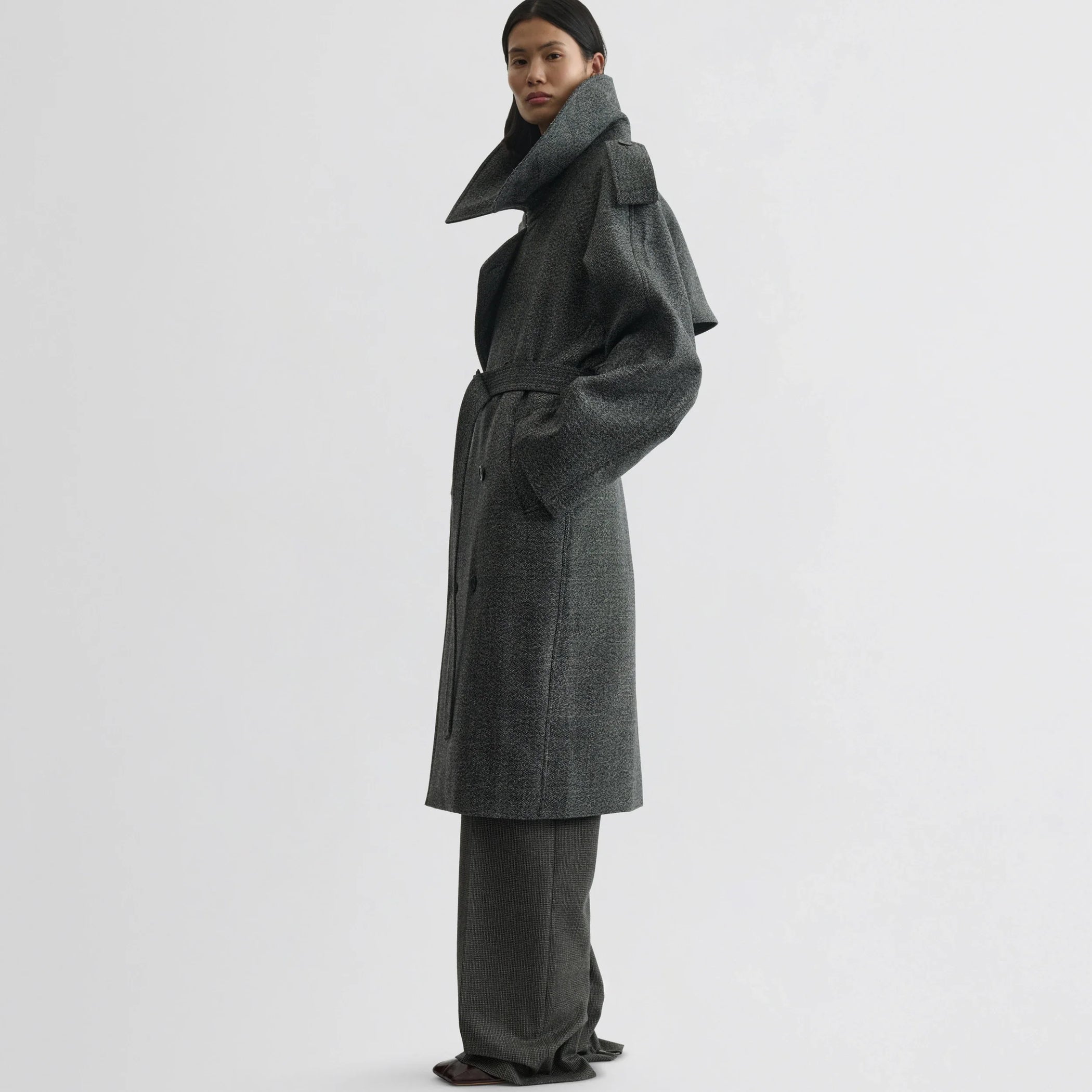 Side view of model wearing padded trench coat in salt and pepper wool.