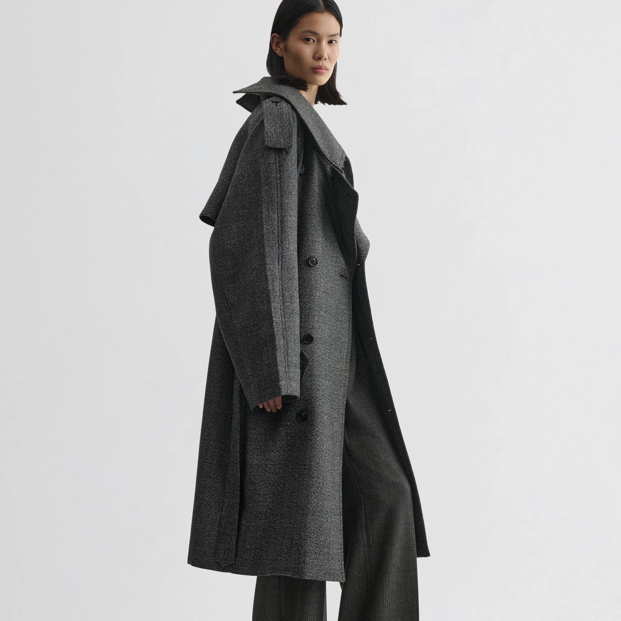 Side view of model wearing padded trench coat in salt and pepper wool.