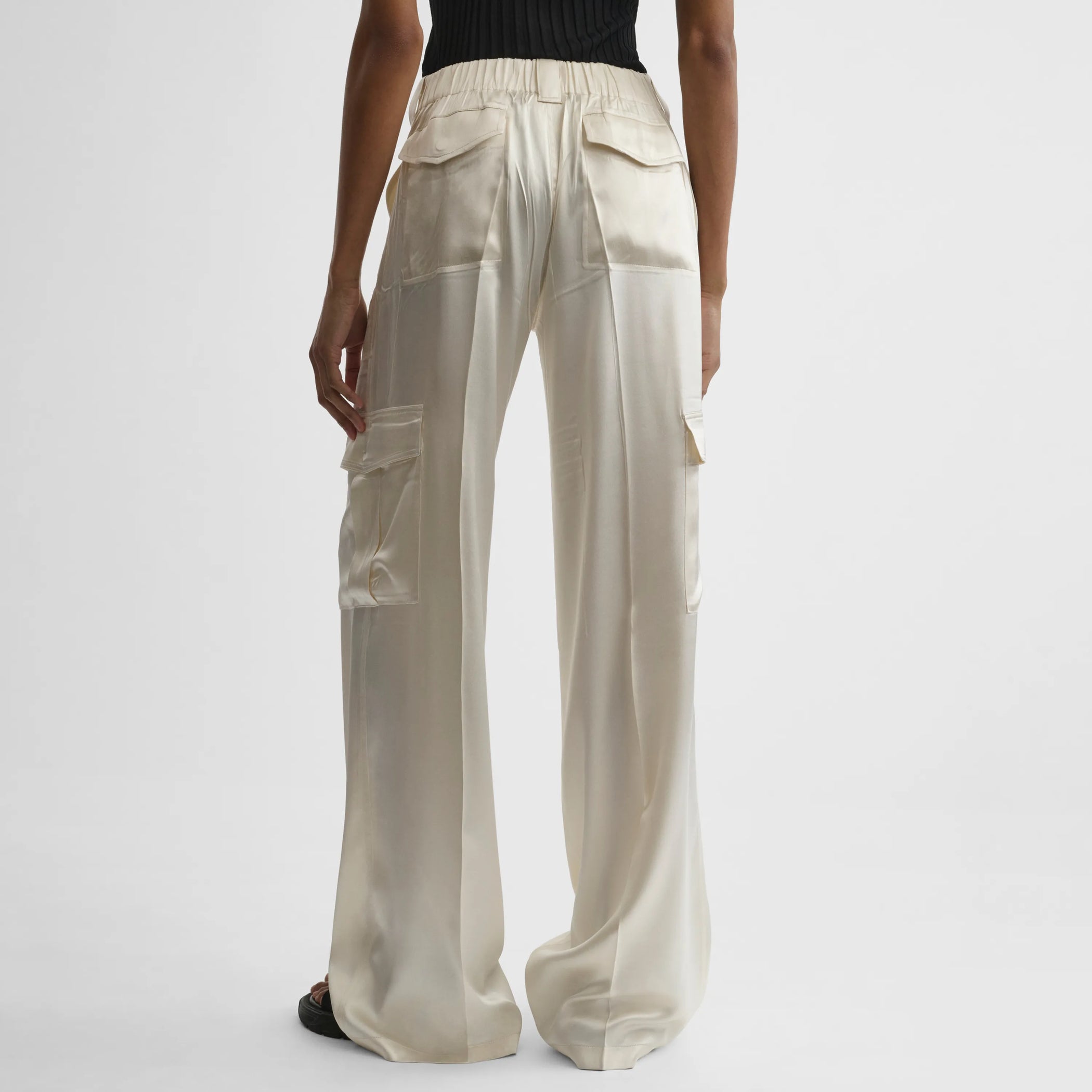 Back view of model wearing liquid cargo trousers in cream silk satin.
