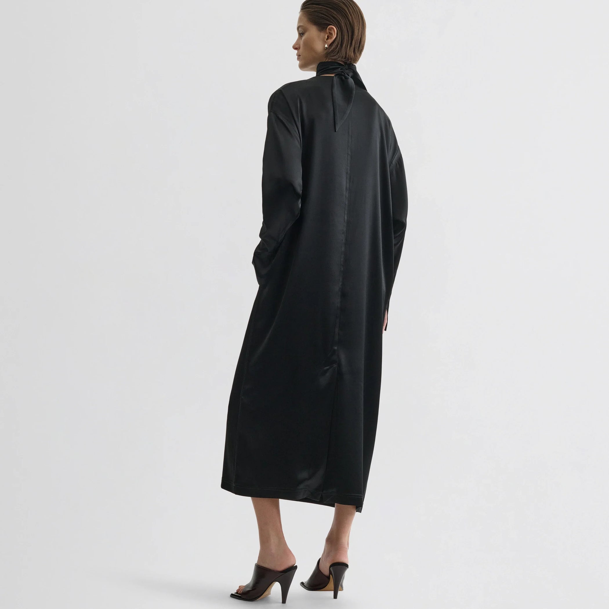 Back view of model wearing liquid high neck dress in black silk.