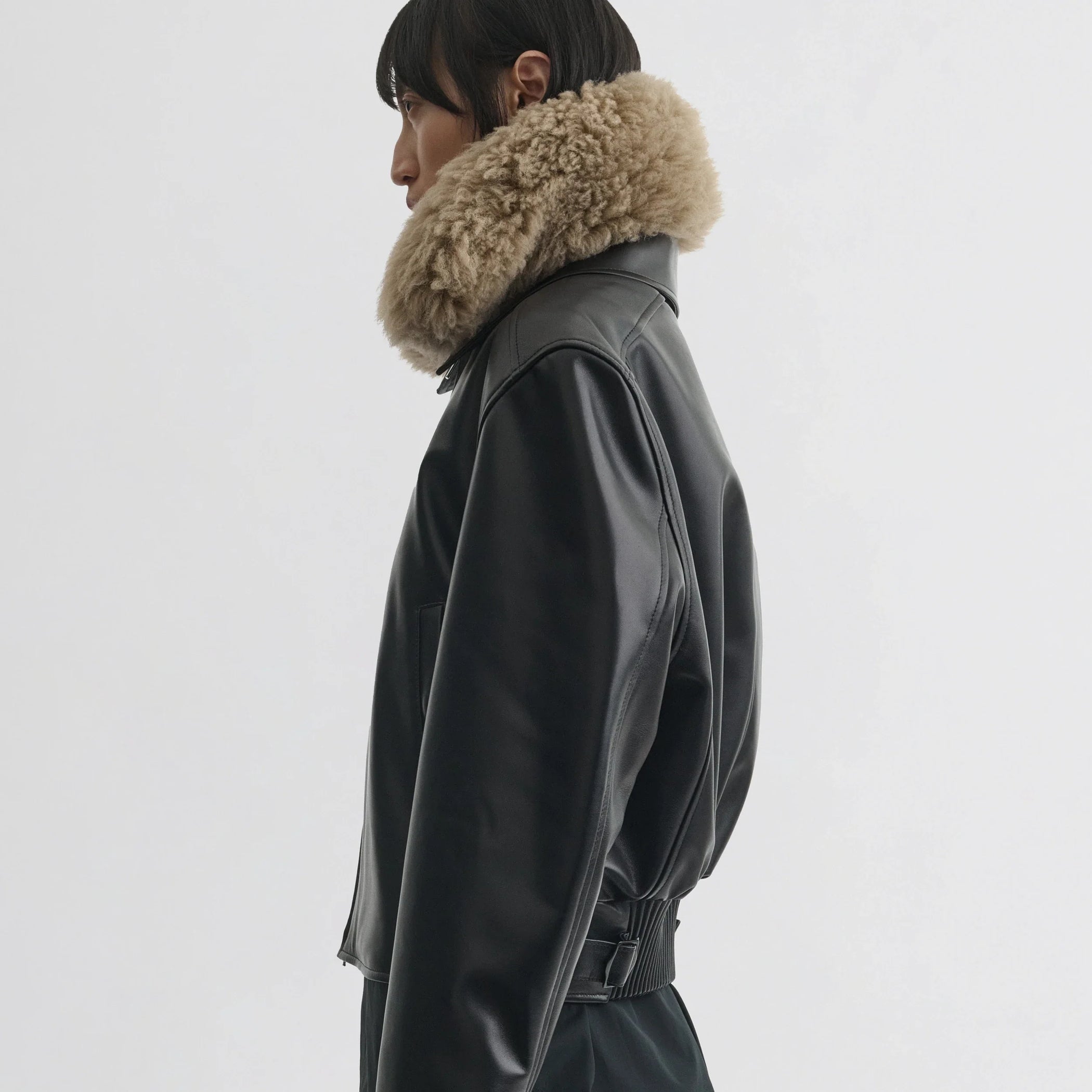 Side view of model wearing cropped aviator jacket in black leather.