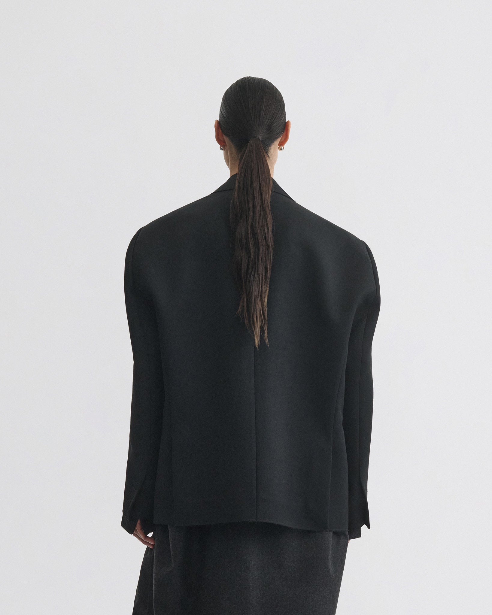Back view of model wearing tuxedo jacket in black wool
