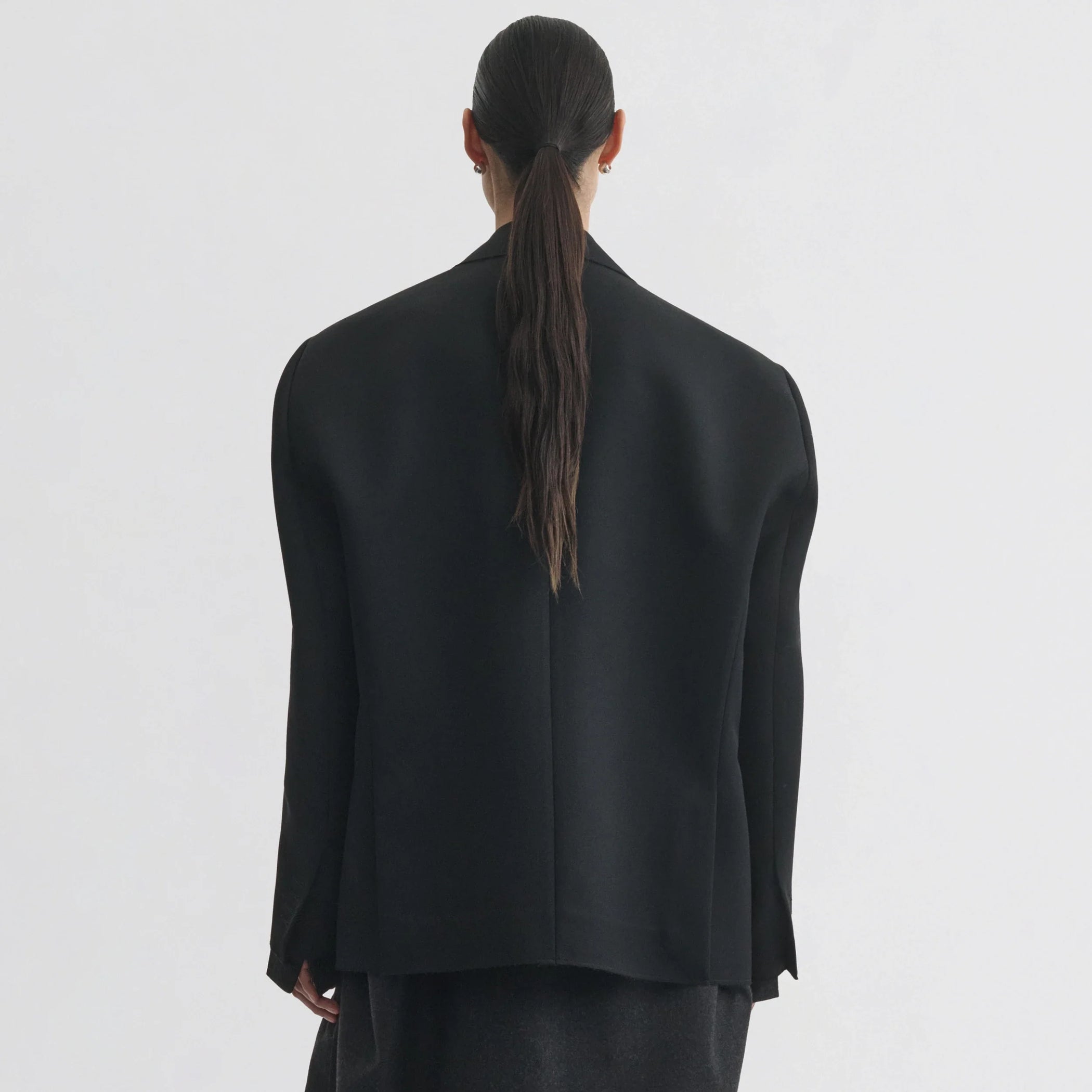 Back view of model wearing tuxedo jacket in black wool.
