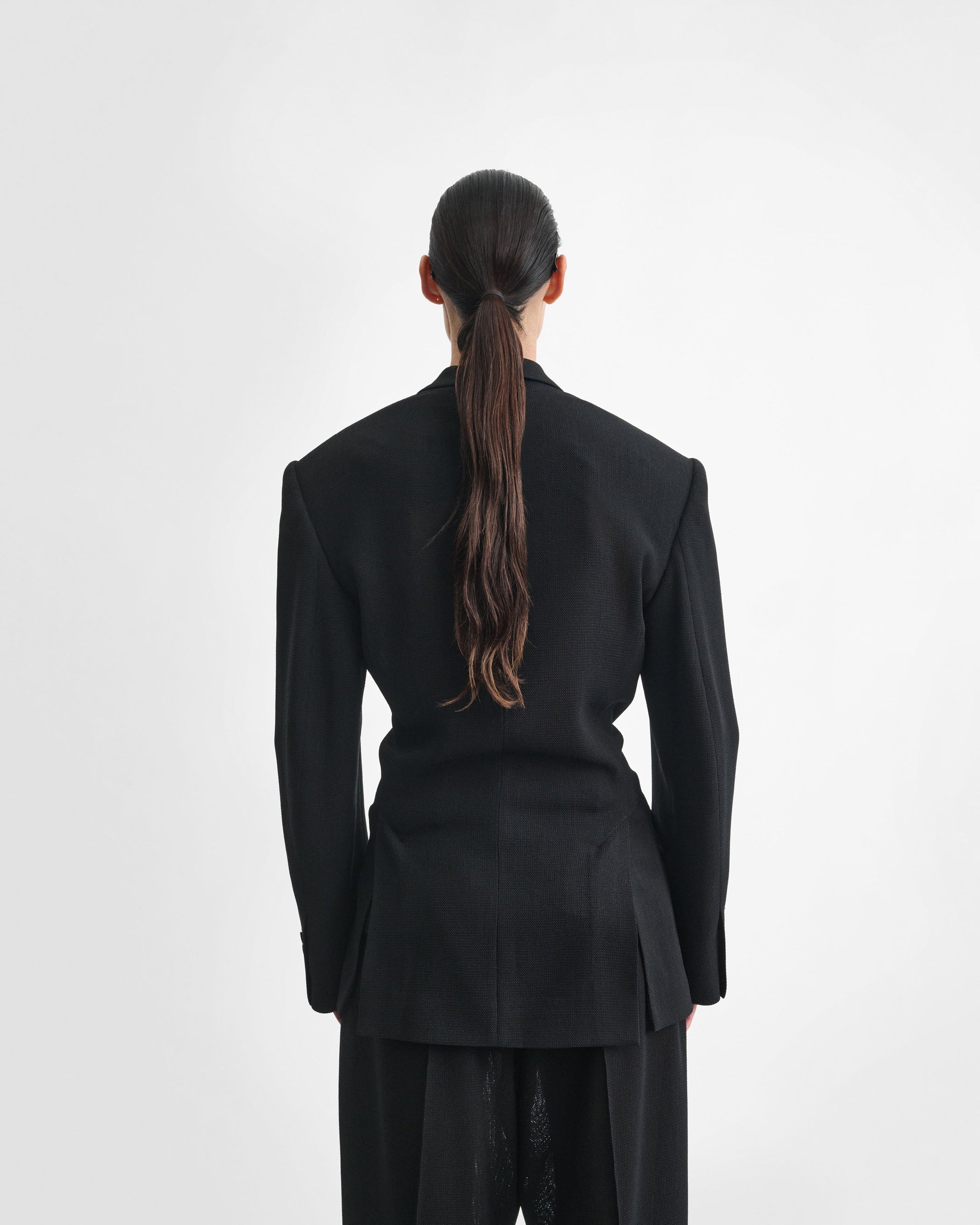 Back view of model wearing CINCHED TAILORED JACKET in black woven viscose